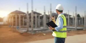 A construction worker with a clipboard examines a building site, part of a Civil Surveyor Course.